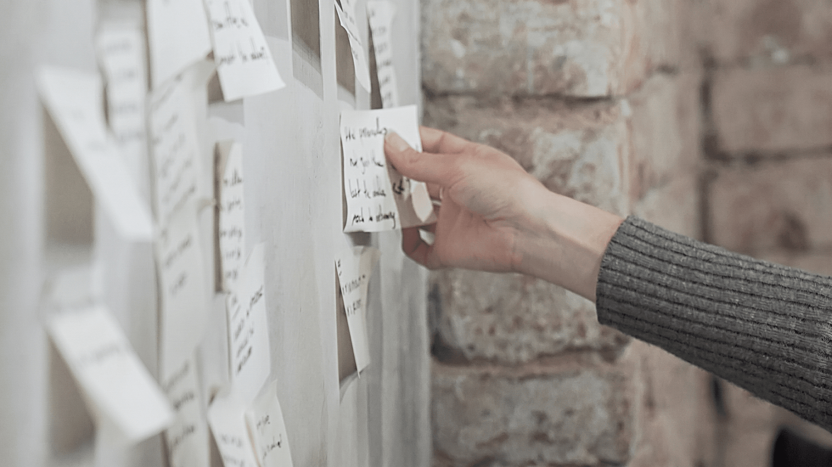 A hand pinning handwritten idea notes to a wall during a sprint